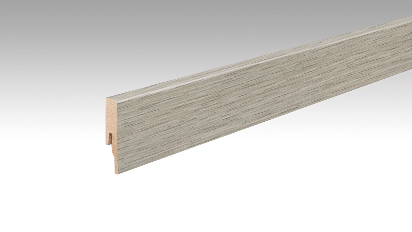 Eine lange, rechteckige Fußleiste mit Holzstruktur in einem hellen, grauen Eichenfarbton, eine Nut auf der Rückseite.