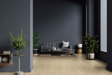 Modernes Wohnzimmer mit dunkelgrauer Couch, cremefarbenem Kissen, Couchtisch, Teppich, mehreren großen Zimmerpflanzen, Stehlampe, Beistelltisch mit Vase und Bücherregal an dunkelgrauer Wand, heller Holzboden.