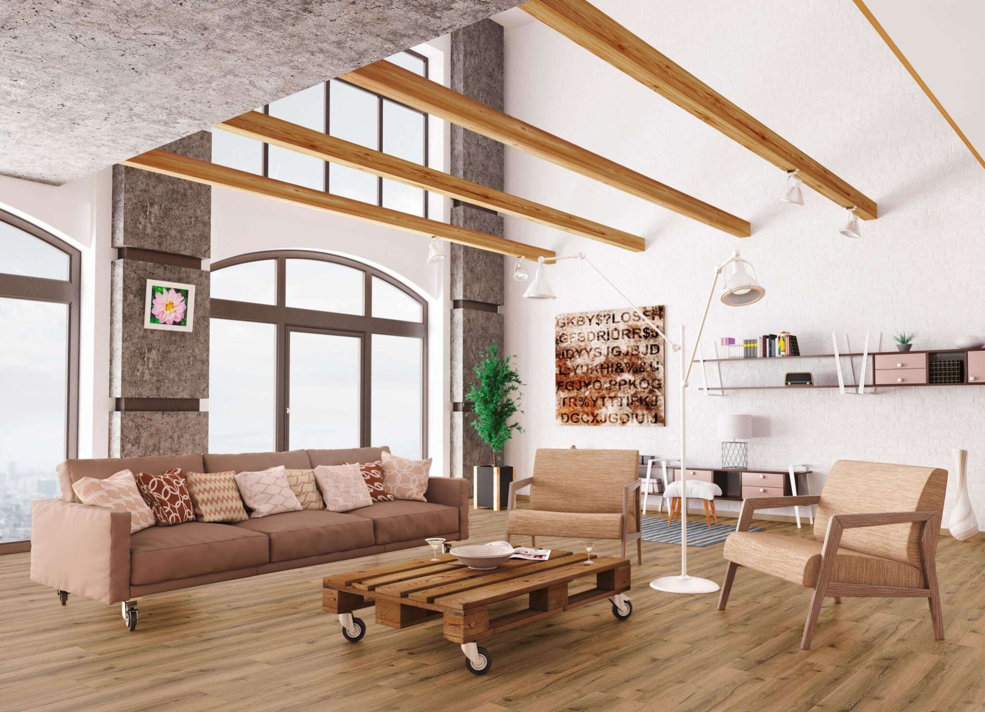 Helles Wohnzimmer mit braunem Sofa und gemusterten Kissen, zwei beige Sesseln, Couchtisch aus Paletten auf Rollen, Stehlampe, Regal mit Büchern und Dekoration, Pflanze, große Fenster, Deckenbalken aus Holz, Wandbilder, Parkettboden.