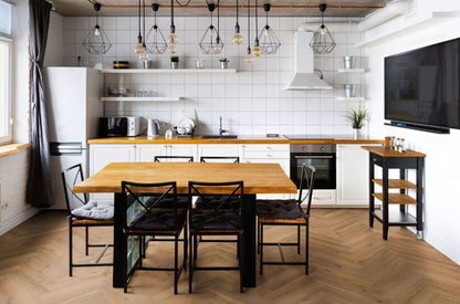 Moderne Küche mit Holztisch, sechs Stühlen mit Polsterung, weißem Kühlschrank, Wandregalen, Backofen, Mikrowelle, Wasserkocher, Spüle, Topfpflanzen, Hängelampen, Küchenwagen, großer Flachbildfernseher, weiß geflieste Wand.