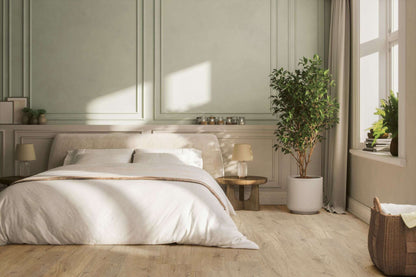 Helles Schlafzimmer mit großem Bett, weißer Bettwäsche, zwei Nachttischen mit Lampen, großer Topfpflanze, Korb und Fenstersims mit Büchern und Pflanze.