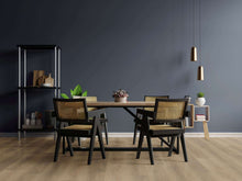 Esszimmer mit vier Holzstühlen mit Geflecht, rechteckigem Holztisch, Regal mit Pflanzen und Deko, zwei goldenen Pendelleuchten.