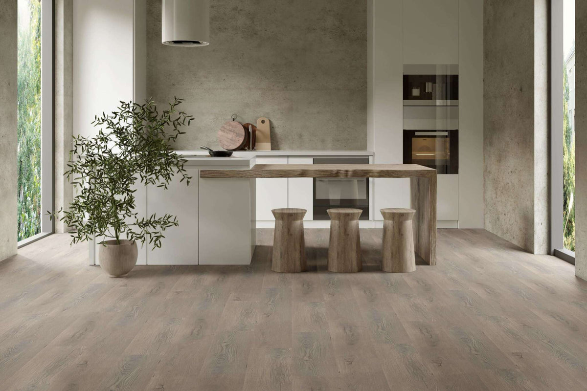 Moderne Küche mit hellen Fronten, Kücheninsel und massiver Holztheke, drei Holz-Hocker, große Fenster, Topfpflanze links, Wand mit Betonoptik, eingelassener Backofen, Dunstabzugshaube, Schneidebretter und Pfanne auf Arbeitsplatte.