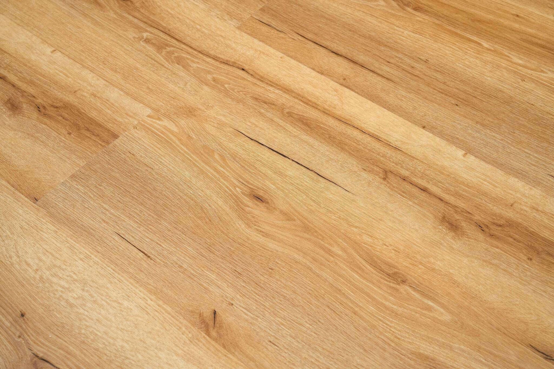 Bodenbelag aus mehreren breiten, hellbraunen Paneelen mit sichtbarer Holzmaserung und feinen dunklen Linien. Die Paneele sind gleichmäßig verlegt und erinnern an Eichenholz mit natürlichen Ast- und Musterstrukturen. Die Oberfläche wirkt glatt und gepflegt und vermittelt einen warmen, einladenden Eindruck.