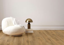 Weißer gepolsterter Sessel mit weißer Decke, daneben goldene Tischlampe auf gestapelten Büchern, Holzboden, weiße Wand.