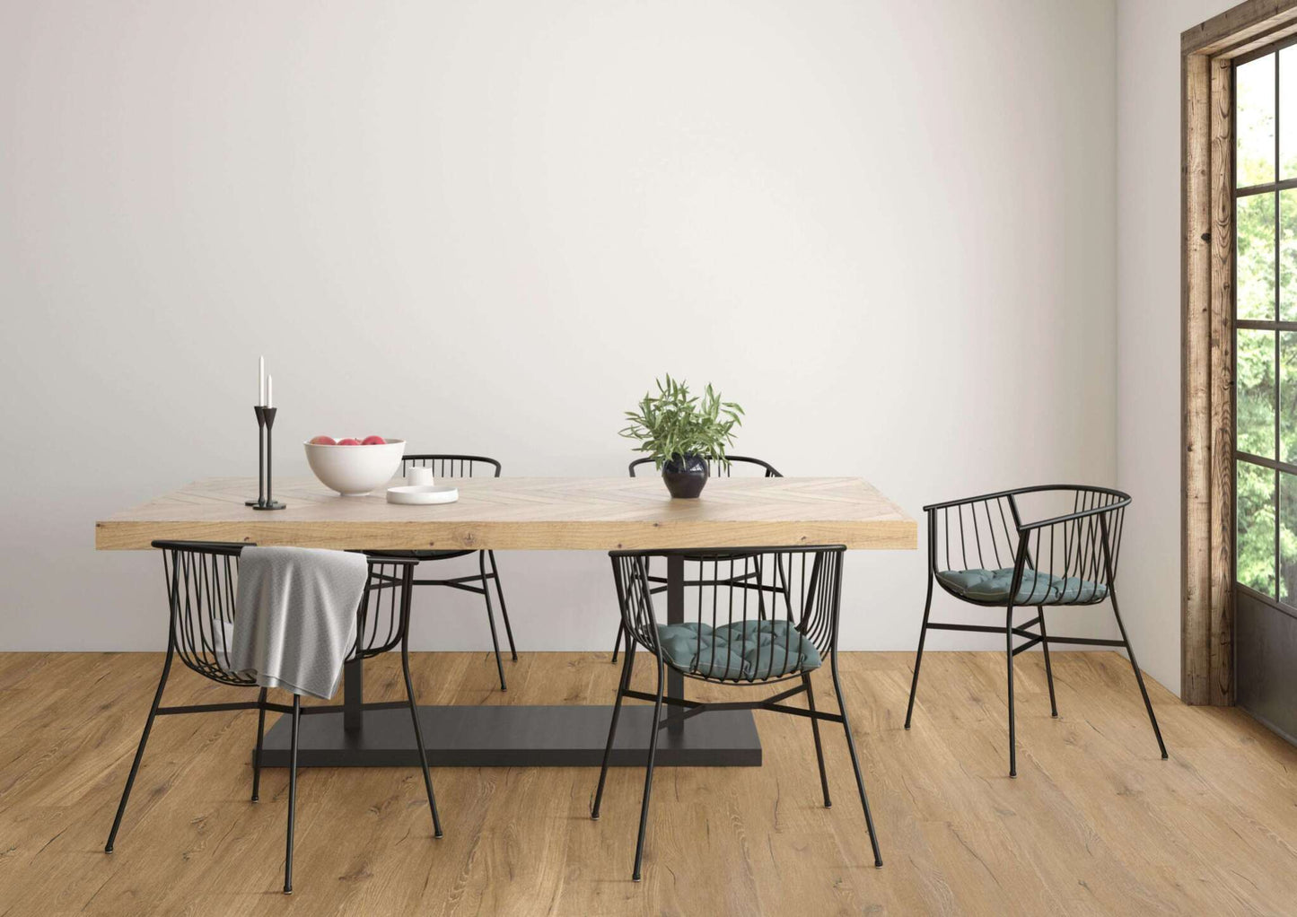 Holztisch mit schwarzem Metallgestell, fünf schwarze Stühle mit Drahtgestell, graue Decke, grüne Sitzkissen, kleine Pflanze, weiße Schale mit Äpfeln, schwarze Kerzenhalter mit weißen Kerzen, Fensterrahmen aus Holz, heller Raum, Holzboden.